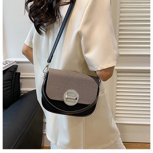 Detail of a brown textured and black leather crossbody bag with a round silver clasp