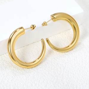 Polished chunky gold hoop earrings hanging on minimalist white geometric jewelry stand