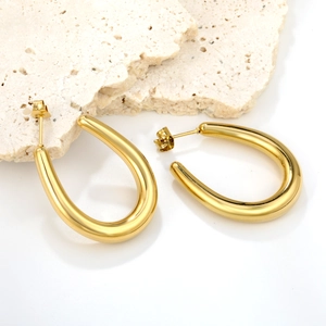 Macro detail of high-polished 18K gold U-shaped earrings on natural stone props