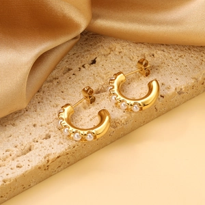 Boucles d'oreilles créoles dorées en C avec perles blanches sur une surface en pierre