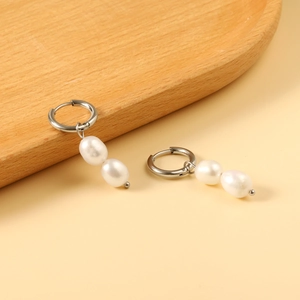 Dettaglio di orecchini con doppie perle e cerchi in argento su vassoio in legno