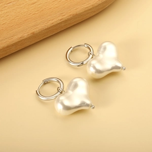 Dettaglio di orecchini di perle a cuore con cerchi in argento su superficie beige