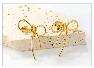 Close-up of golden bow-shaped stud earrings on travertine stone with a polished finish