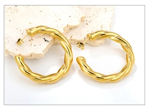 Close-up of golden 18K twisted hoop earrings with a polished spiral texture and a C-shaped design