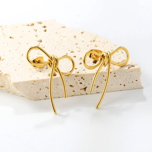 Elegant gold polished stainless steel bow stud earrings displayed on a travertine stone
