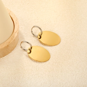 Polished oval 18k gold earrings with silver hoops on a minimalist textured surface