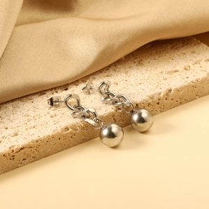 Close-up of stainless steel drop earrings with bead charms on a textured stone stand