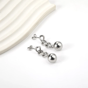 Detail of silver chain stud earrings with metal ball pendants on a minimalist background