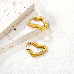 Détail de boucles d'oreilles cœur en or avec perles blanches sur un support en pierre