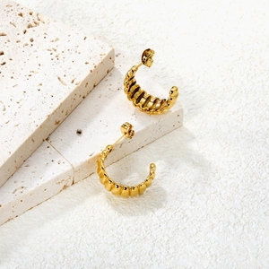 Détail de boucles d'oreilles créoles dorées texturées posées sur pierre de travertin