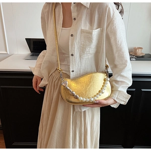 Detail of gold wrinkled moon bag with large pearls and silver chain worn by model