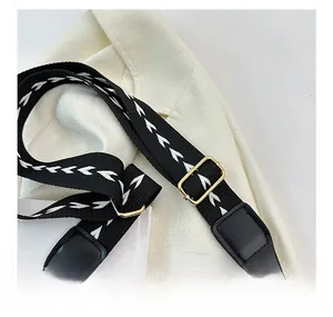 Detail of adjustable black shoulder strap with white embroidery and gold metal clips