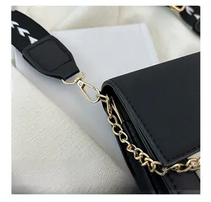 Detailed close-up of golden hardware hooks and wide printed strap on black leather bag