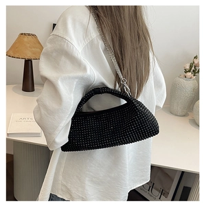 Detail of a black beaded handbag with silver snake chain worn by a model in a modern home