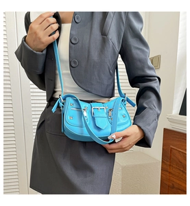 Detail of blue Y2K baguette bag with silver studs and zippers on a gray blazer model