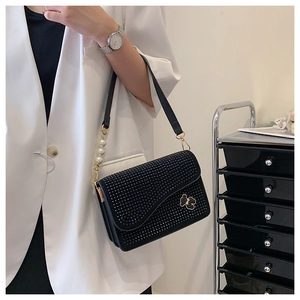 Detail of black rhinestone shoulder bag featuring gold bear charm and pearl strap