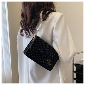 Detail of black rhinestone velvet handbag with pearl strap on model in white blazer