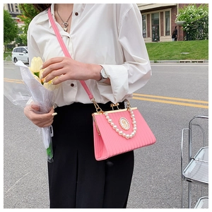 Detail of pink vintage evening bag with pearl chain and golden relief badge emblem