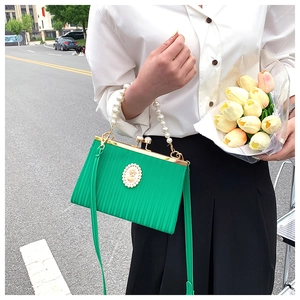 Detail of green pleated evening bag featuring pearl handle and vintage crest decoration