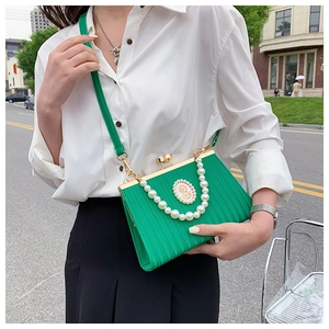 Detail of green textured leather evening bag with pearl badge and gold clasp closure