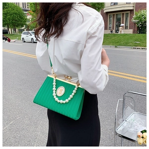 Detail of emerald green pleated evening bag with pearl badge and gold clasp