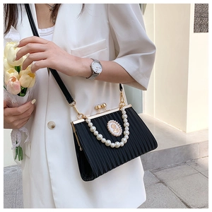 Detail of black pleated clutch bag with pearl handle and vintage emblem on gold hardware