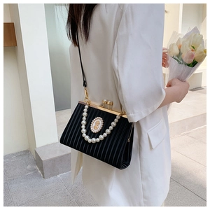 Detail of elegant black pleated handbag with pearl handle and golden emblem on white suit