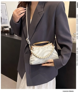 Detail of white wavy shell bag with metal frame, pearl handle and leather shoulder strap