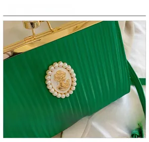 Détail de la pochette de soirée verte avec texture verticale et emblème en perles brodé