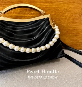 Close-up of black pleated shell bag with gold metal handle and faux pearl strap detail
