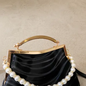 Detail of black shell clutch with gold curved handle and decorative pearl strap accent