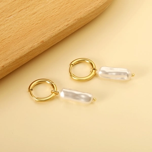 Elegant gold hoop earrings with elongated white pearl drops on a warm background