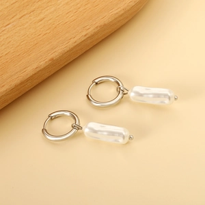 Minimalist silver stainless steel hoop earrings with long white pearl drops on beige background