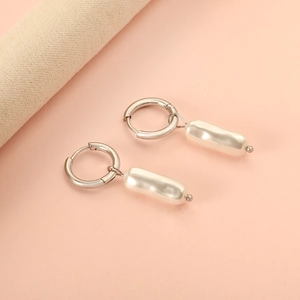 Macro detail of silver hoop earrings with elegant hanging white long-shaped pearls