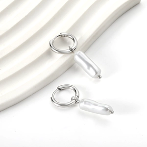Close-up of silver hoop earrings with long baroque white pearls on a textured stand