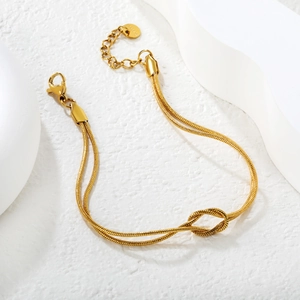 Detail view of golden double-layer snake chain bracelet with knot design and lobster clasp