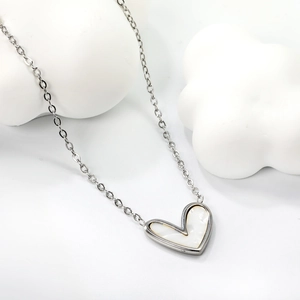 Gros plan détaillé d'un collier avec pendentif cœur argenté sur fond blanc épuré