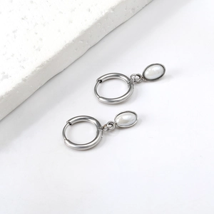 Macro detail of silver oval pearl earrings on a textured stone surface, minimalist design