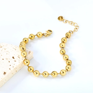 Close-up of a minimalist golden bead bracelet with adjustable lobster clasp and round tag