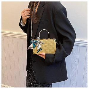 Detail of golden box clutch bag with vertical texture and decorative silk scarf handle