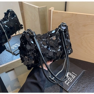 Detail of elegant black sequin handbag with woven straps on a mirror surface