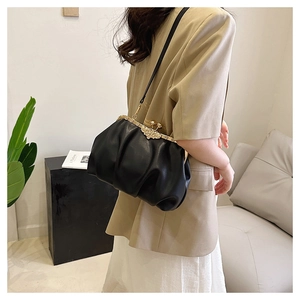 Detail of black pleated cloud bag with vintage gold floral clasp on elegant beige suit