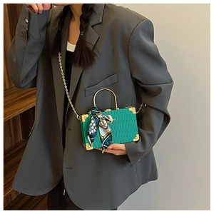 Detail of green rigid box bag featuring gold metal handle and decorative silk scarf