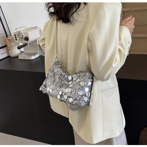 Detail of silver sequin handbag with metal chain strap shown in a modern cafe setting
