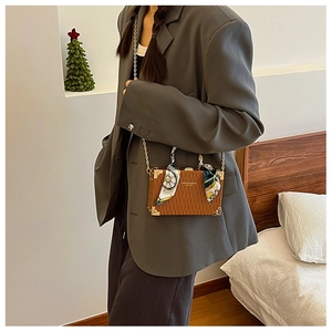 Detail of a brown box bag with gold metal corners, chain strap and a printed silk scarf