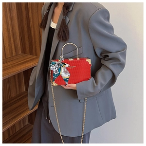 Detail of red accordion-style box bag with golden circular handle and silk scarf decor