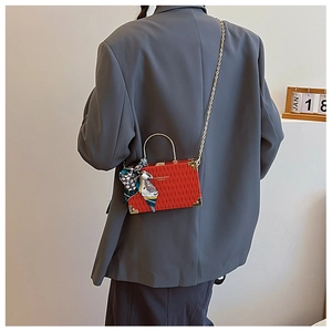 Detail view of red mini box bag with gold metal handle and floral silk scarf accessory