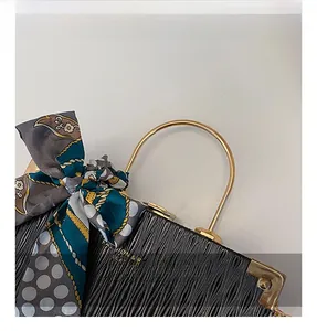 Close-up of black pleated texture handbag with gold metal handle and decorative silk scarf