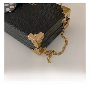 Detail of black epi leather box bag with gold metal corners and chain strap