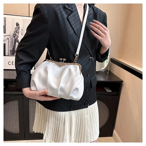 Close-up of white pleated dumpling bag with vintage floral metal clasp and slim strap